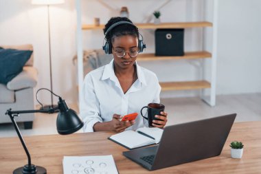 Evden çalışıyorum. Beyaz gömlekli Afrikalı Amerikalı genç bir kadın..