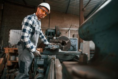Fabrika makinesiyle çalışmaya odaklanmış. Üniformalı işçi içeride..