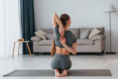 Dayanıklılık egzersizleri. İnce vücutlu ve yoga elbiseli genç bir kadın evde..