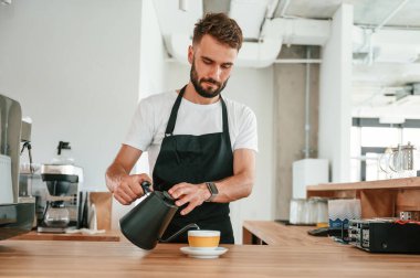 Kahve hazır. Malı bardağa döküyorum. Beyaz gömlekli ve siyah önlüklü kafe çalışanı içeride..