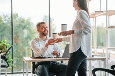 Ellerinde içkiler olan bir fincan. Erkek ve kadın modern ofiste birlikte çalışıyorlar..