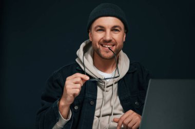 Gülümsüyor ve dizüstü bilgisayarın başında oturuyor. Yakışıklı adam stüdyoda arka planda..