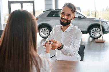 Masanın başında oturup anahtarları almak. Beyaz elbiseli bir adam araba galerisinde birlikte..