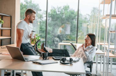 Bacakları masanın üzerinde otururken. Erkek ve kadın modern ofiste birlikte çalışıyorlar..