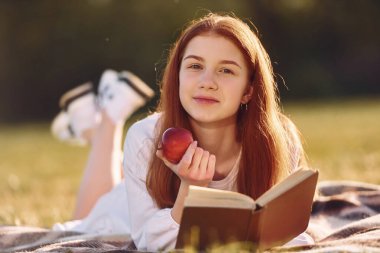 Bir kitap ve bir elmayla. Genç kız güneşli bir günde sahada güzel bir hafta sonu geçiriyor..