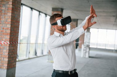 Eller yukarı! İnşaat alanında resmi kıyafetli bir adam VR oyunu oynuyor..