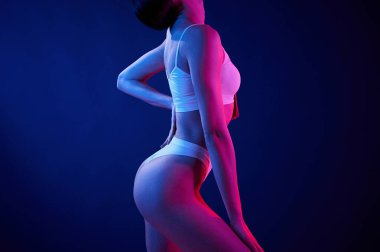 Yan görüş. İç çamaşırlı genç kadın stüdyoda neon ışıklarıyla bekliyor..