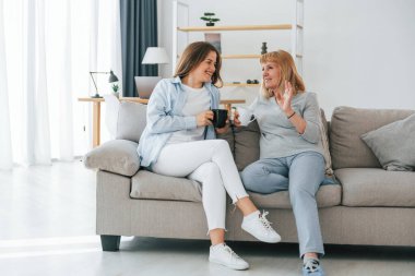 Bir bardak içkiyle, sohbet ederek. Anne ve kızı evde birlikteler..