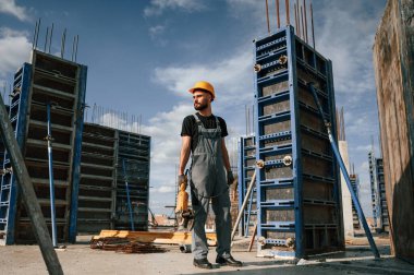 Elinde öğütme makinesiyle dikiliyorsun. Üniformalı adam inşaat alanında çalışıyor..