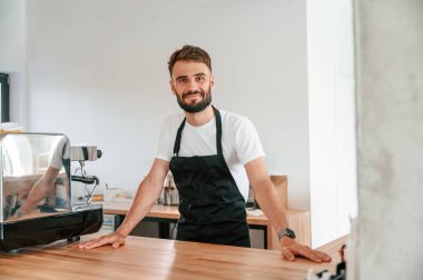 Beyaz gömlekli ve siyah önlüklü kafe çalışanı içeride..