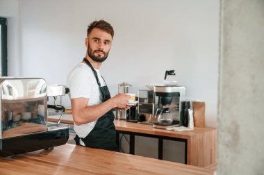 Bir fincan kahveyle. Beyaz gömlekli ve siyah önlüklü kafe çalışanı içeride..