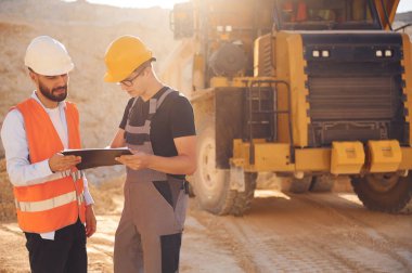 Nakliye kamyonunun yanında durup belgelerden bahsetmek. Üniformalı iki adam taş ocağında birlikte çalışıyor..