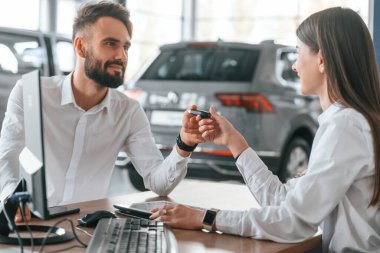 Yeni otomobilin sahibi anahtarlarını alıyor. Beyaz elbiseli bir adam araba galerisinde birlikte..
