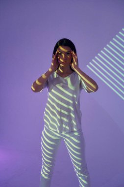 Mor renkli arka plan. Yeşil renkli çizgiler. Stüdyoda projektör neon ışıkları altında güzel genç bir kadın var..