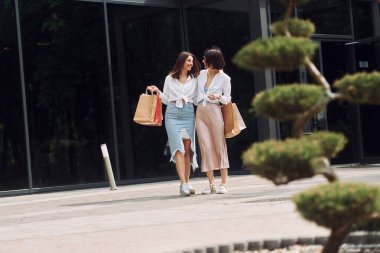 Yakın modern bina. İki bayan arkadaşın alışveriş günü var. Dışarıda çantalarla dolaşmak..