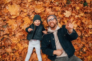 Düşen yapraklarla kaplı yerde yatıyordu. Baba ve küçük oğlu gündüz vakti dışarıda beraberler..