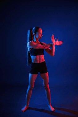 Spor egzersizleri için hazırlanıyorum. Egzersizleri ısıt. Güzel kaslı kadın stüdyoda neon ışıklı..