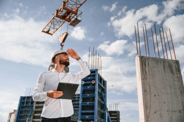 Mühendis not defteri tutuyor. Üniformalı adam inşaat alanında çalışıyor..