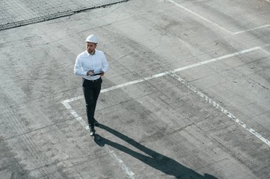 Resmi kıyafetli ve elinde tabletle yürüyen beyaz şapkalı bir adam..