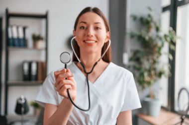 Elinde steteskopla. Beyaz önlüklü güzel bayan doktor ofiste..