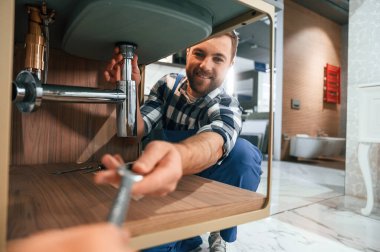 İngiliz anahtarı alıyorum. Mavi üniformalı tesisatçı banyoda çalışıyor..