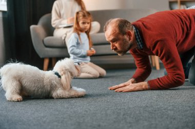 Numara yapıyor. Adam malta köpeğiyle oynuyor. Anne ve kızı izliyor..