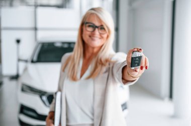 Otomobil sahibi anahtarları tutuyor. Beyaz elbiseli kadın araba galerisinde..
