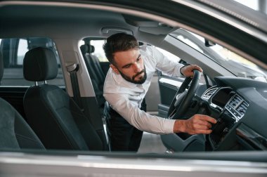 Otomobilin salonunu inceliyorum. Beyaz elbiseli genç adam araba galerisinde..