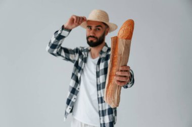 Şapkalı turist elinde baget ekmeği tutuyor. Yakışıklı adam stüdyoda beyaz arka plana karşı..