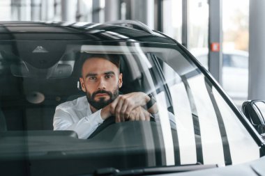 Ön manzara. Otomobilin içinde oturuyor. Beyaz elbiseli genç adam araba galerisinde..