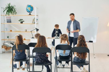 Masadaki mikroskop ile çocuğa bakıyorum. Okulda öğretmenle birlikte bir grup çocuk öğrenci..