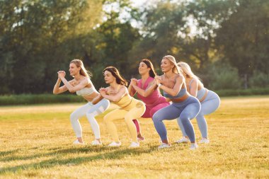 Bacak egzersizi yapıyorum. Bir grup kadın sahada birlikte spor yapıyorlar..