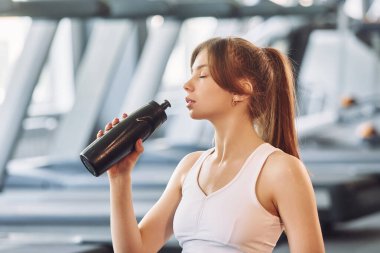 Bir şişe su. Spor elbiseli genç bir kadın spor salonunda spor yapıyor..
