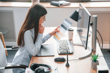 Görüş açısı. Bilgisayarın başında oturuyor. Genç bayan tasarımcı modern ofiste..