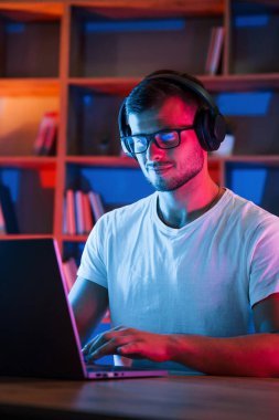 İşine odaklan. Gözlüklü ve beyaz gömlekli bir adam karanlık odada dizüstü bilgisayarın yanında oturuyor..