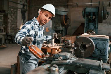 Tamirci fabrika makinesiyle çalışıyor. Üniformalı depo çalışanı içeride..