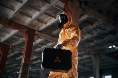 Alt manzara. Kıyamet sonrası binanın harabelerinde kimyasal koruma kıyafeti giymiş bir adam..