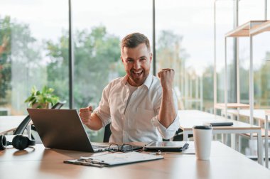 Başarılı bir proje. Kutlama ve mutluluk kavramı. Resmi kıyafetli adam modern ofiste çalışıyor..