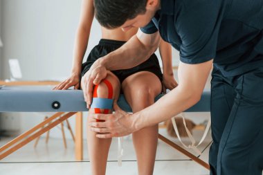 Bacaklarla çalışmak. Cilde Kinesio bandı yapıştıran bir kadın fizyolog..