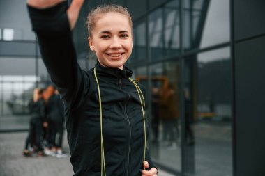 Selfie yapıyorum. Bir grup sportif kadın dışarıda, siyah binanın yakınında..
