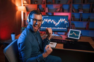 Happy borsa simsarı içeride bilgisayar başında çalışıyor ve başarıyı kutluyor. Değişim ve para kavramı.