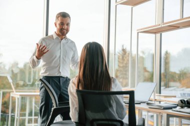 Birbirleriyle konuşuyorlar. Erkek ve kadın modern ofiste birlikte çalışıyorlar..