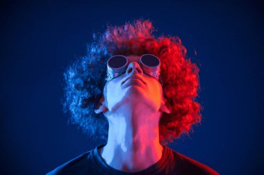 Neon ışıkla aydınlatılmış kıvırcık saçlı genç adamın portresi. Eski moda gözlüklerle..