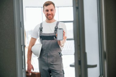 Elinde akıllı telefonla. Tamirci modern odada kapalı duruyor..