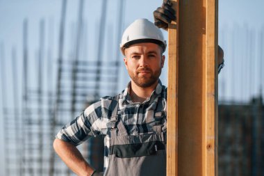 Ciddi adam ayakta duruyor ve poz veriyor. İşçi gündüz vakti şantiyede..