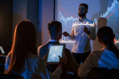 Komisyoncu projeksiyonla ilgili planı gösteriyor. Erkek lider borsa şirketinde çalışanlarla konuşuyor..