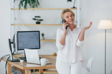 İletişim kurmak için akıllı telefonu kullanmak. Resmi giyimli kadın borsacı ofiste çalışıyor..