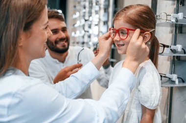 Aile bir arada. Kadın, erkek ve küçük kız görüşü düzeltmek için doğru gözlüğü seçiyor..