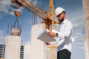 Planı ellerindeyken. Üniformalı adam inşaat alanında çalışıyor..