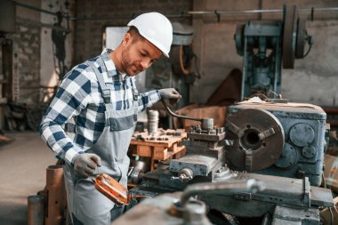 Tamirci fabrika makinesiyle çalışıyor. Üniformalı depo çalışanı içeride..